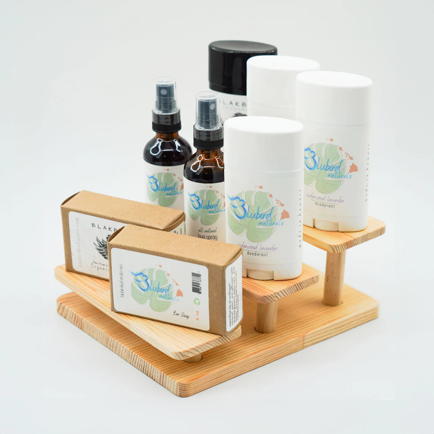 Natural skincare products display featuring Bluebird Naturals deodorant, bug spray, and handmade soap, and Blakbird organic soap on a wooden stand, eco-friendly personal care items for sensitive skin.